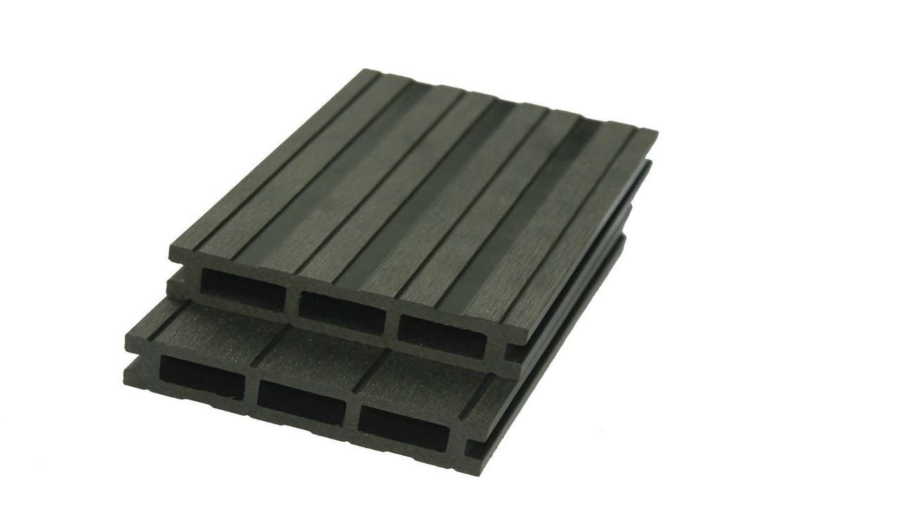 Overhead flat-lay photograph of two stacked dark charcoal composite decking boards with ribbed top surface and hollow rectangular chambers, on white background, cool diffused light, slate grey and graphite tones with a modern, architectural mood.